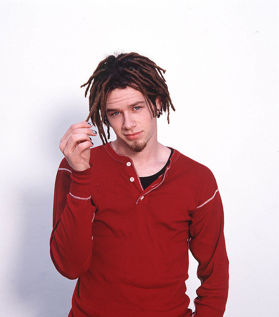 Jacob in a photoshoot wearing a red henley, painted nails, and with dreads 