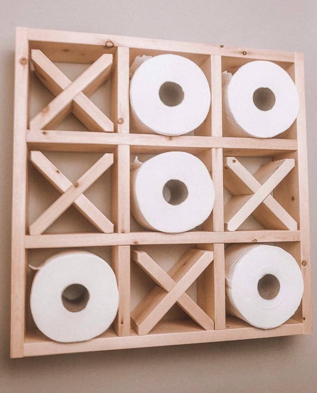 Wood shelf with nine squares. Four are filled with wooden X shapes and the rest are filled with toilet paper rolls. 