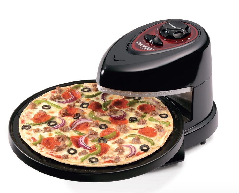 A black rotating pizza oven with a vegetable and pepperoni pizza being cooked on the non-stick rotating pan
