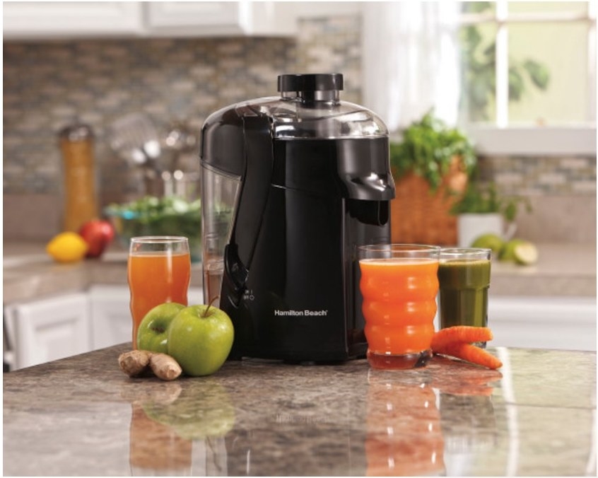 A black Hamilton Beach juicer displayed on the counter next to cups of carrot and green juice