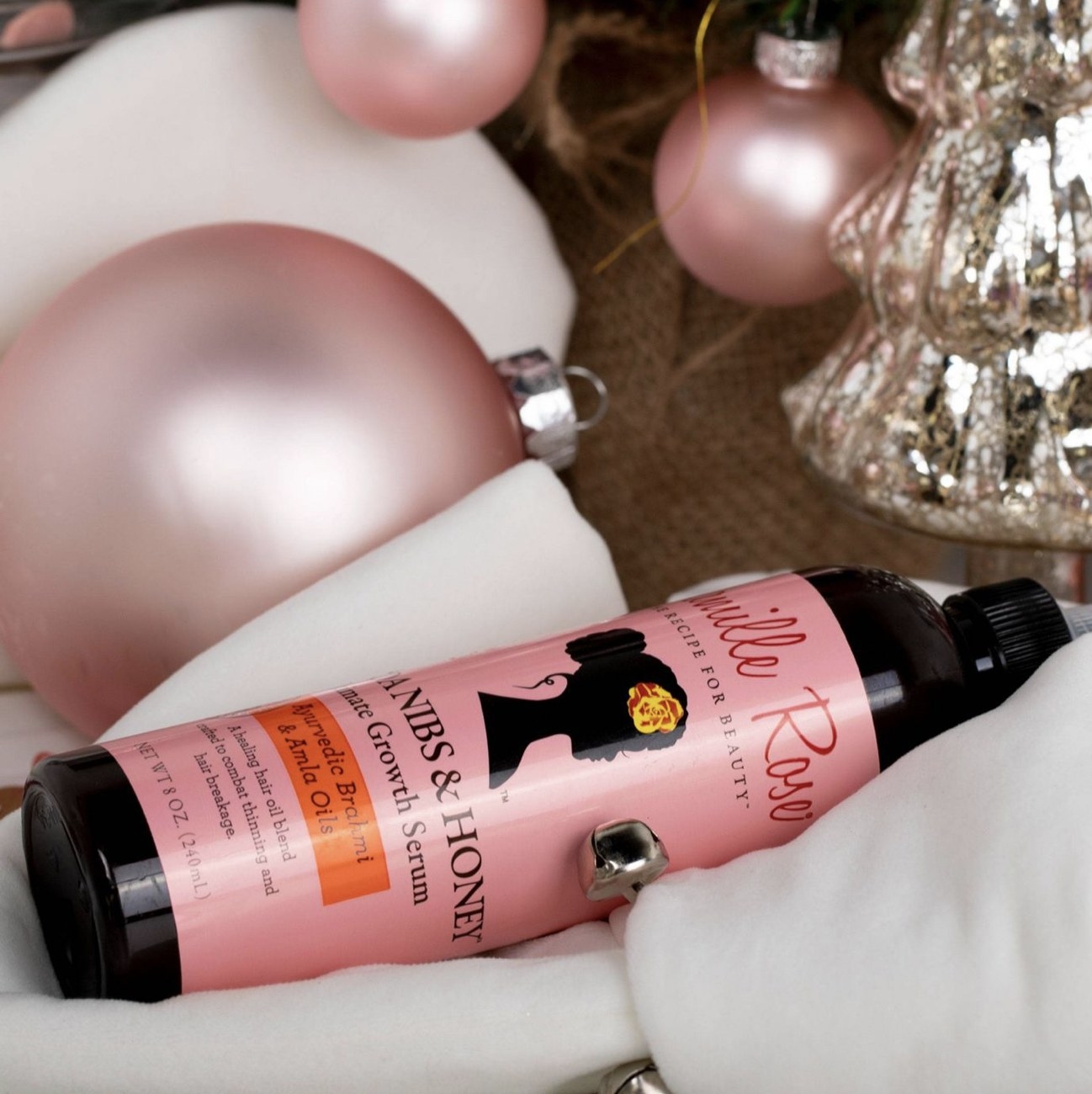 A bottle of hair serum with pink Christmas ornaments.