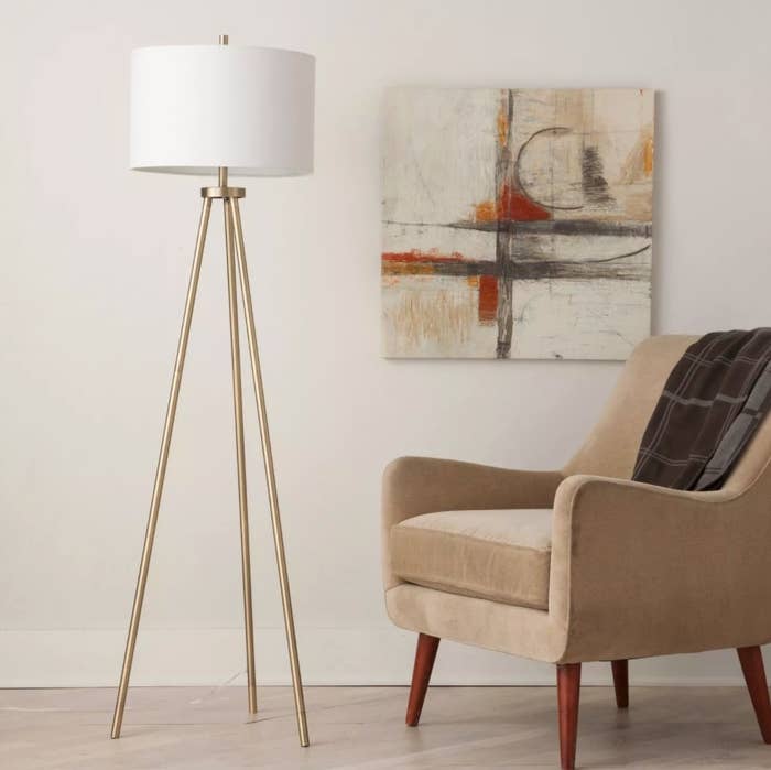 A tripod floor lamp with brass legs and white fabric lampshade