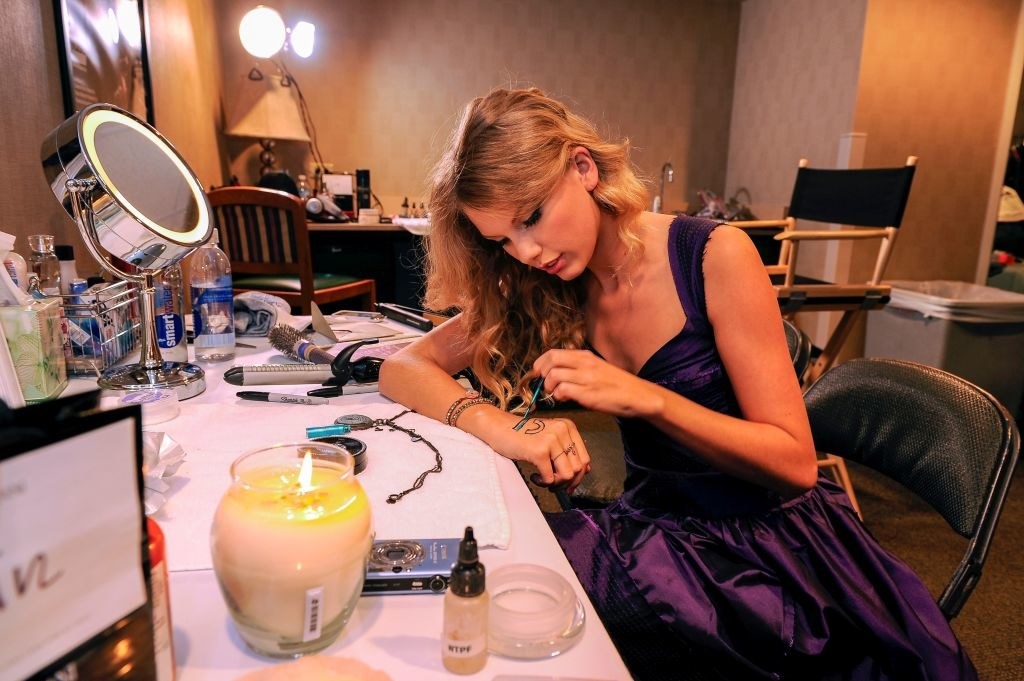 Taylor sitting at a table painting 13 on her hand, with a burning candle and wearing a gown