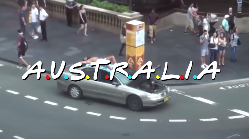 A busy Sydney intersection with a man lying on top of his broken down car with his pants off