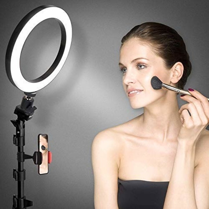 A woman doing her makeup on camera in front of a ring light.