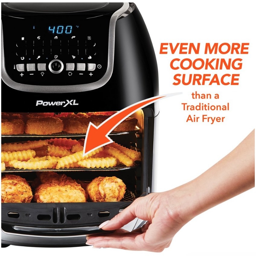 A black, 10 quart air fryer being opened by a models hand displaying crispy fries and tenders inside