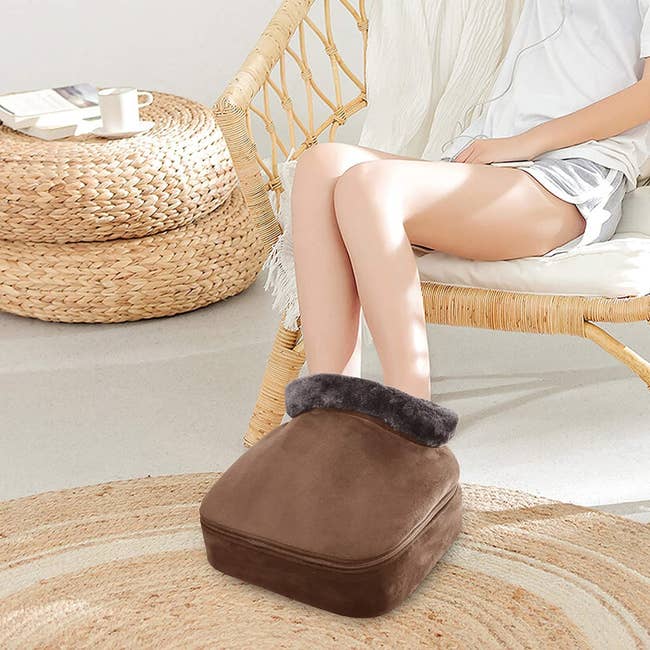 person using a brown foot warmer and massager while sitting in a chair
