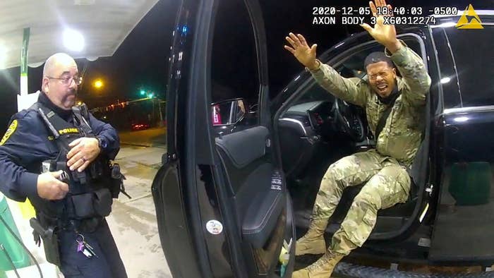 Nazario&#x27;s eyes are closed in response to being pepper-prayed and he has his arms raised as he sits in the driver&#x27;s seat of the car with the door open. A police officer stands on the other side of the door. 