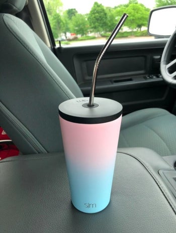 reviewer's two toned insulated tumbler cup with a straw in a car