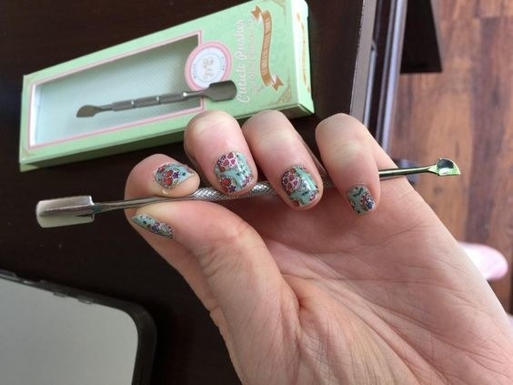 A reviewer holding the pusher and spoon with clean cuticles and painted nails