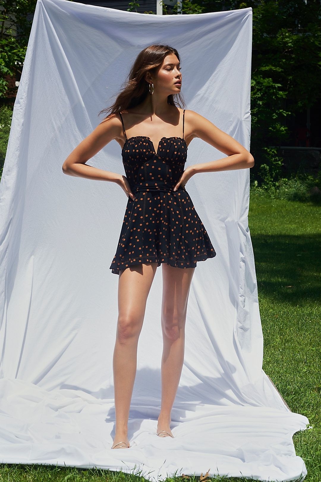 a model wears the spotty dotty mini romper outside in front of a draped white sheet
