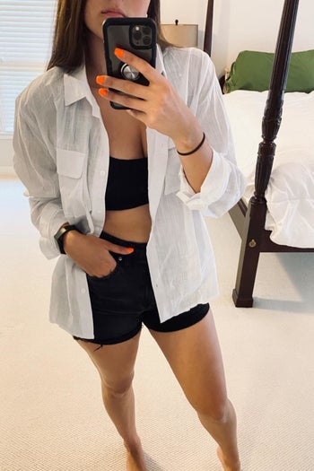 a reviewer selfie of them wearing the white shirt open over a black sports bra and shorts 