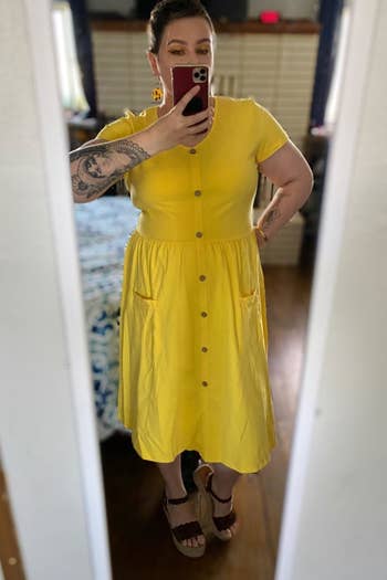 a reviewer mirror selfie of them wearing the yellow short-sleeved midi dress 