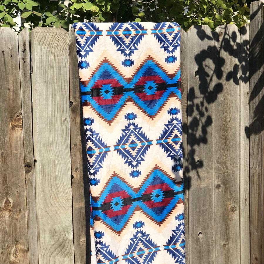 blue, white, tan, and red patterned blanket folded and hangin over a fence