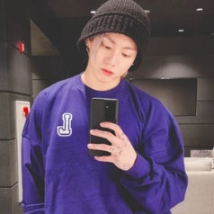 A mirror selfie of Jungkook; he holds his phone and wears a sweater and a beanie