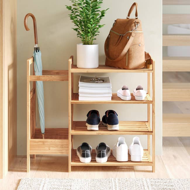 the entry way organizer that has shoes an umbrella a purse a plant and a stack of magazines on it