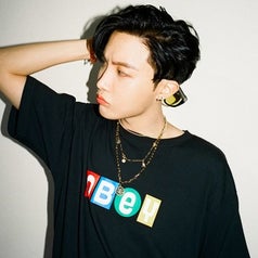 J-Hope poses while looking away from the camera; he has dark hair and wears a t-shirt that says "obey" on it"
