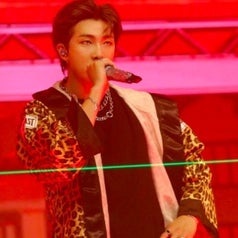 RM wears a leopard print robe and raps into a microphone; the background is red