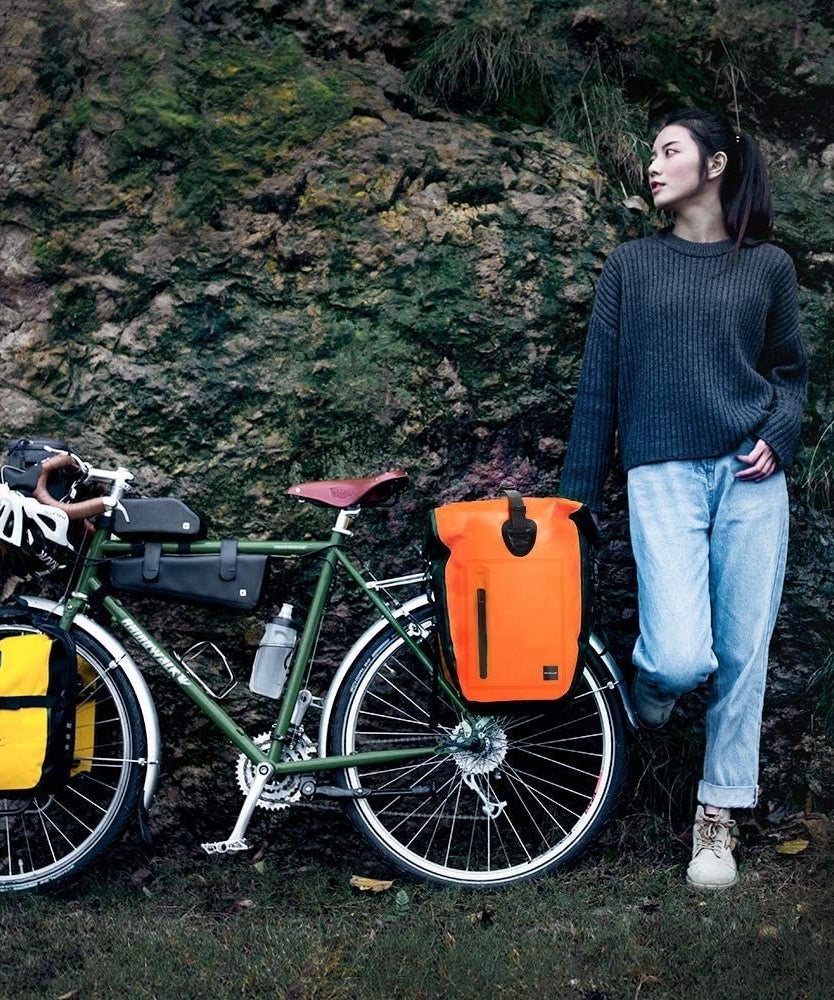 A person posing next to a bike with pannier bags on it 