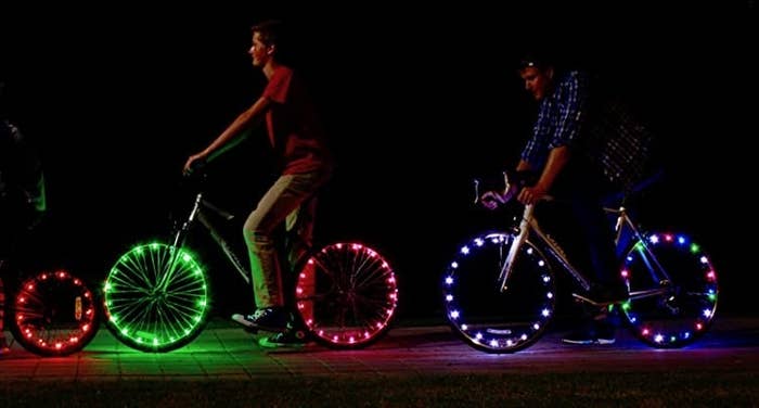 Two people riding bikes in the dark with bright lights on their wheels 