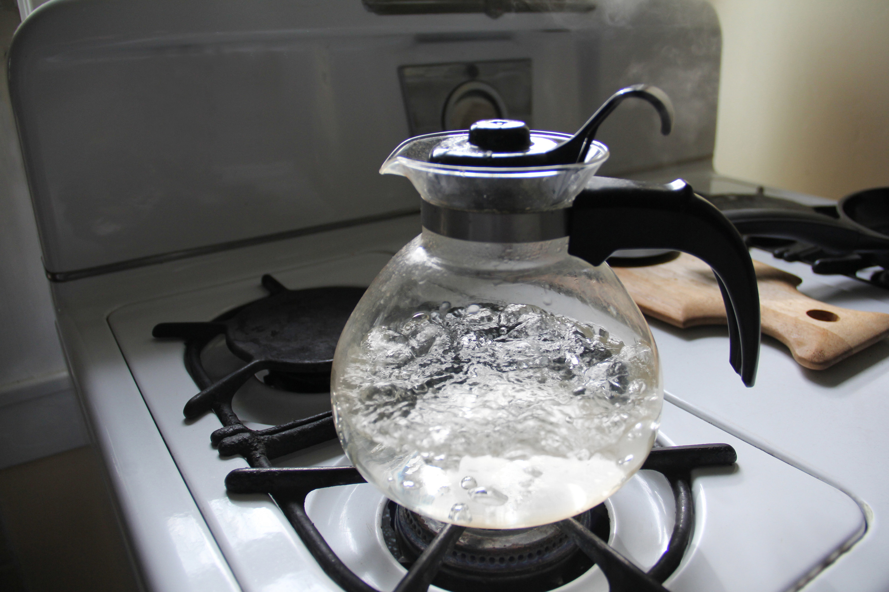 Glass pitcher filled with boiling water atop a stove top