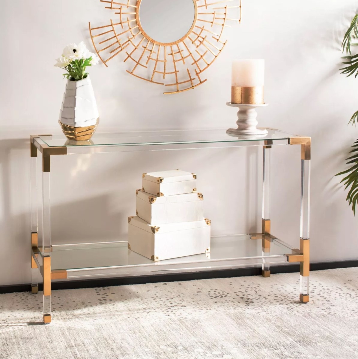 The console table in glass with gold corners holding a vase of flowers and candles