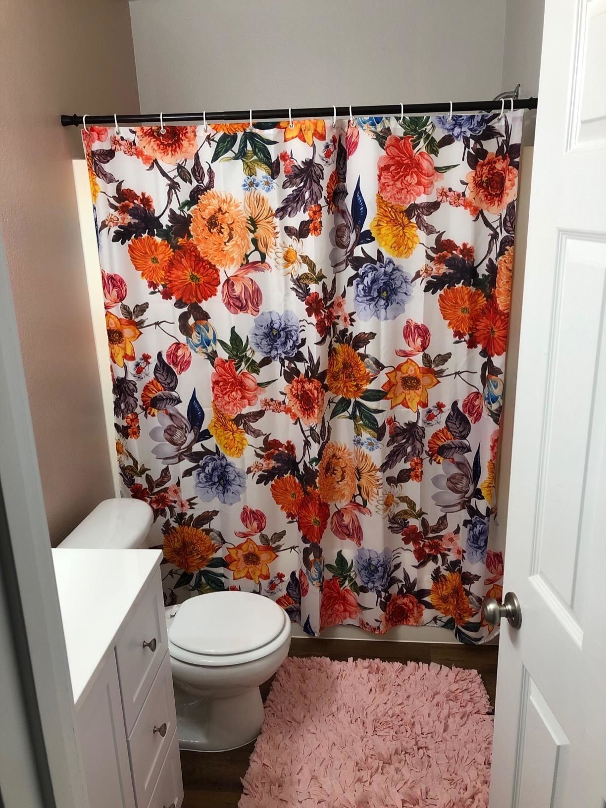 white shower curtain printed with blue, pink, red, yellow, and orange flowers in a reviewer&#x27;s bathroom