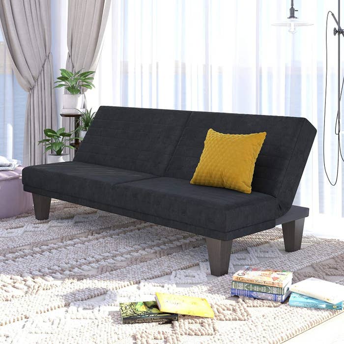 a black angled futon couch with a yellow pillow on it