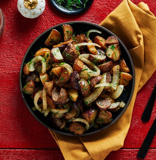 A bowl of quartered, roasted little potatoes sprinkled with parsley, dill, and sliced roasted onion.