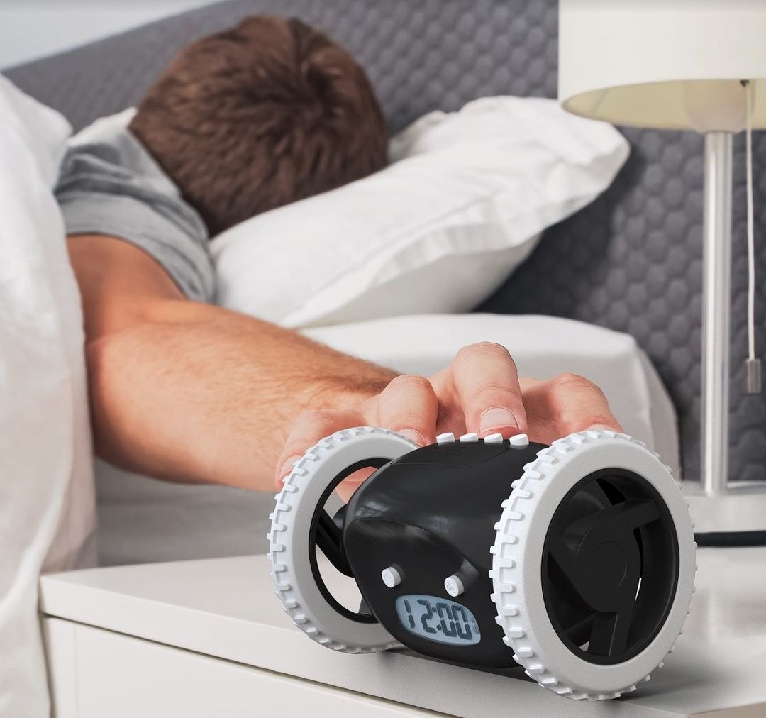 A sleeping person reaching for the rolling alarm clock