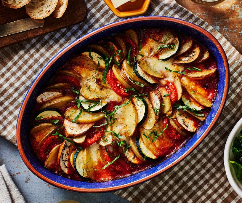 A ceramic baking dish with a beautifully arranged garden vegetable ratatouille, garnished with fresh herbs.