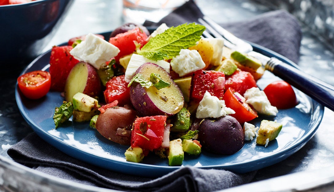 A plate piled with chopped watermelon, little potatoes, avocado, feta, mint, and cherry tomatoes.