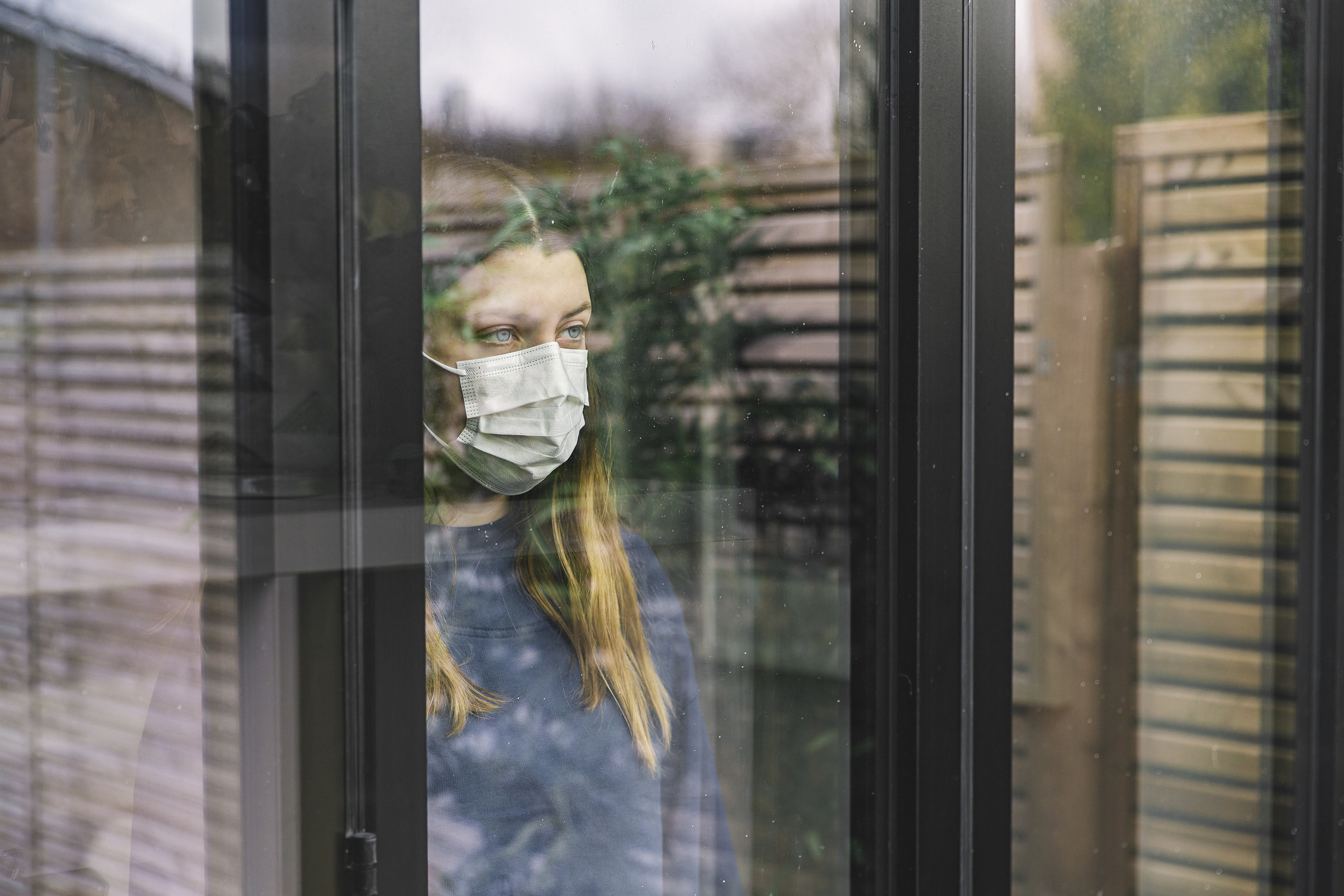 woman in mask looking out a window