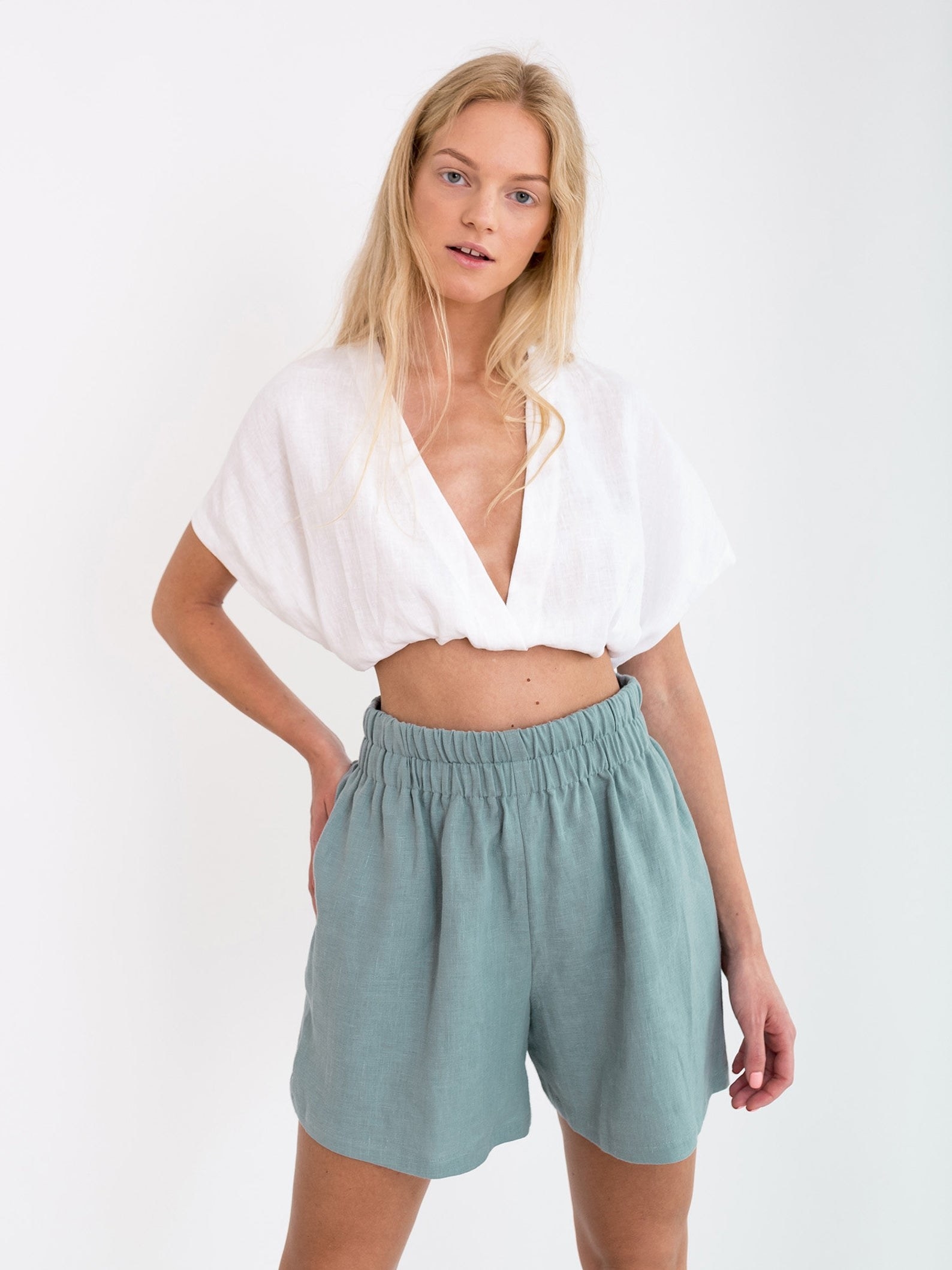 model wearing the dark turquoise isla high waisted linen shorts with a white crop top