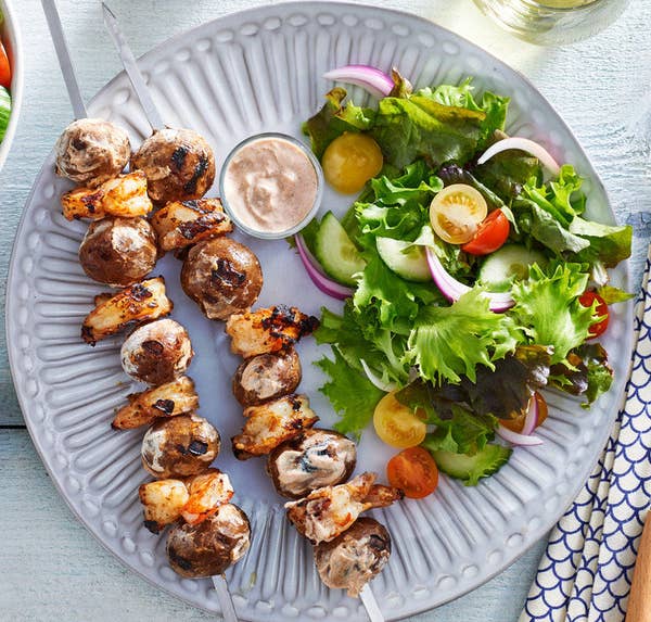 A plate with two shrimp and potato skewers, a bowl of dipping sauce, and a side salad.