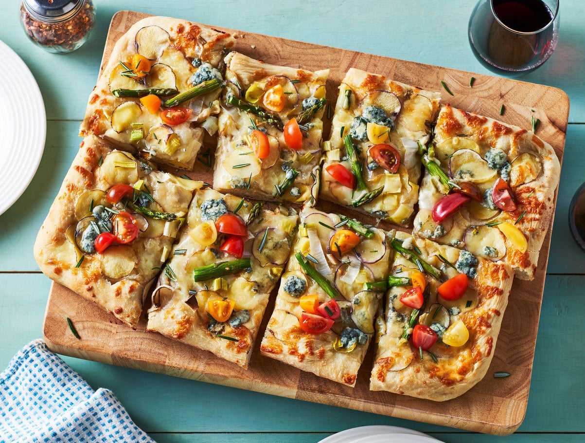 A rectangular pizza topped with potatoes and other vegetables, served on a wooden board.