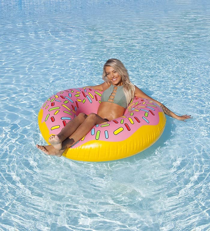 Model floats in pool float that looks like a strawberry-iced donut with red, yellow, blue, and green sprinkles