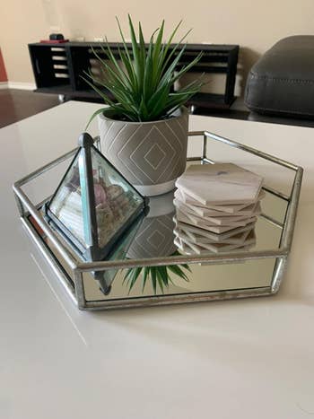 a reviewer's hexagon-shaped silver tray with a mirrored base filled with coasters, a terrarium, and a plant