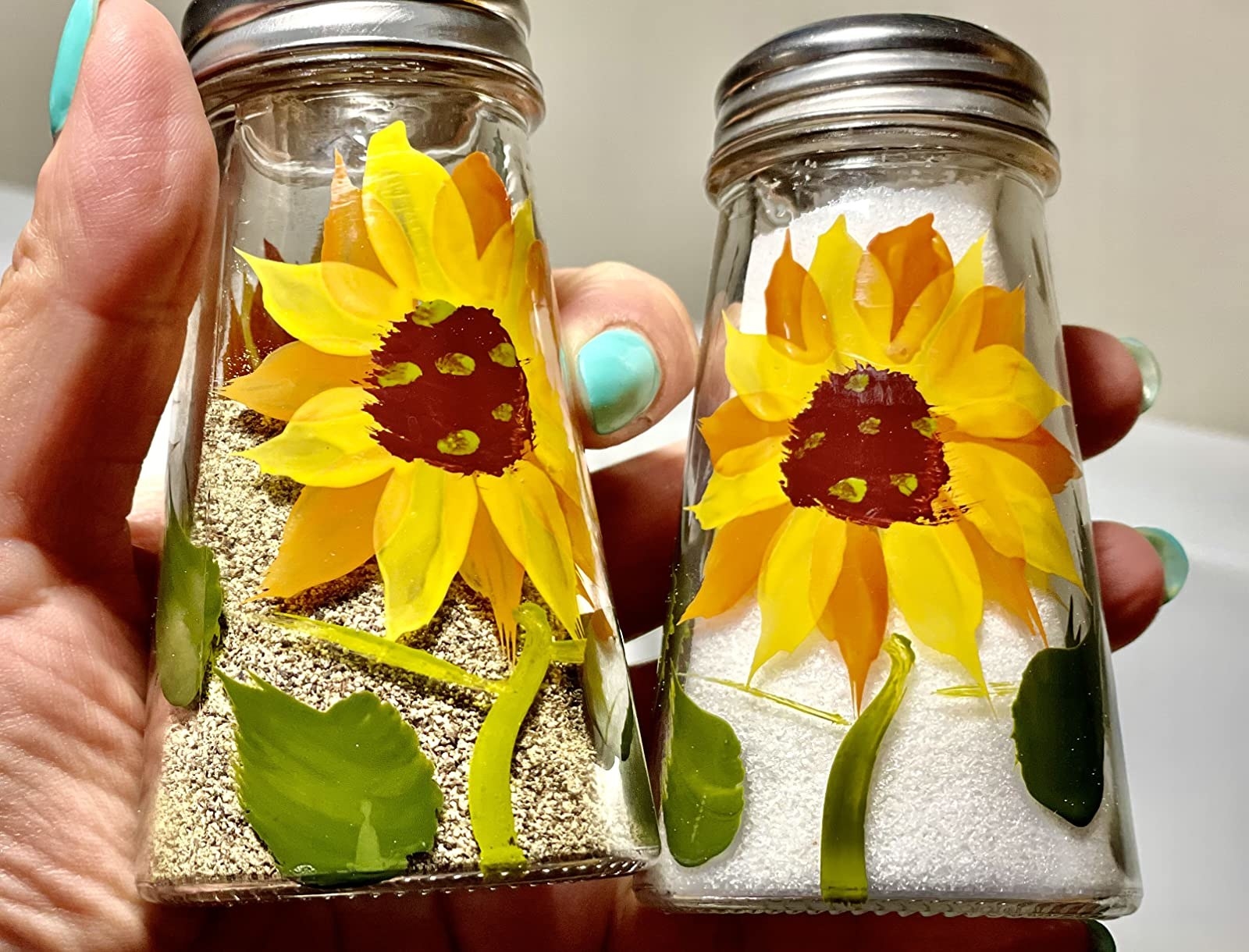 hands holding up the clear shakers with sunflowers painted on