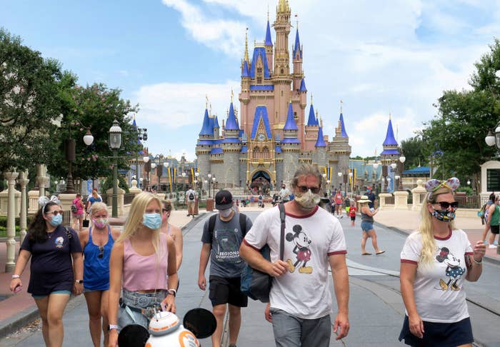 Guests wearing face masks stroll on Main Street in front of Cinderella&#x27;s Castle in Disney World