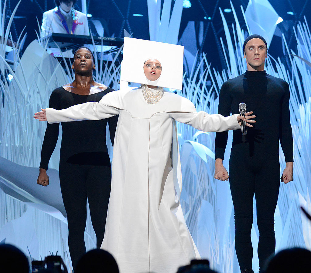 Gaga wearing a white piece of cardboard on her face and a white frock
