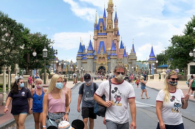 Guests wearing face masks stroll on Main Street in front of Cinderella's Castle in Disney World