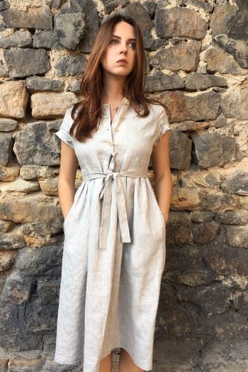 a model wearing a gray linen dress with their hands in the side pockets and a sash-tie belt 