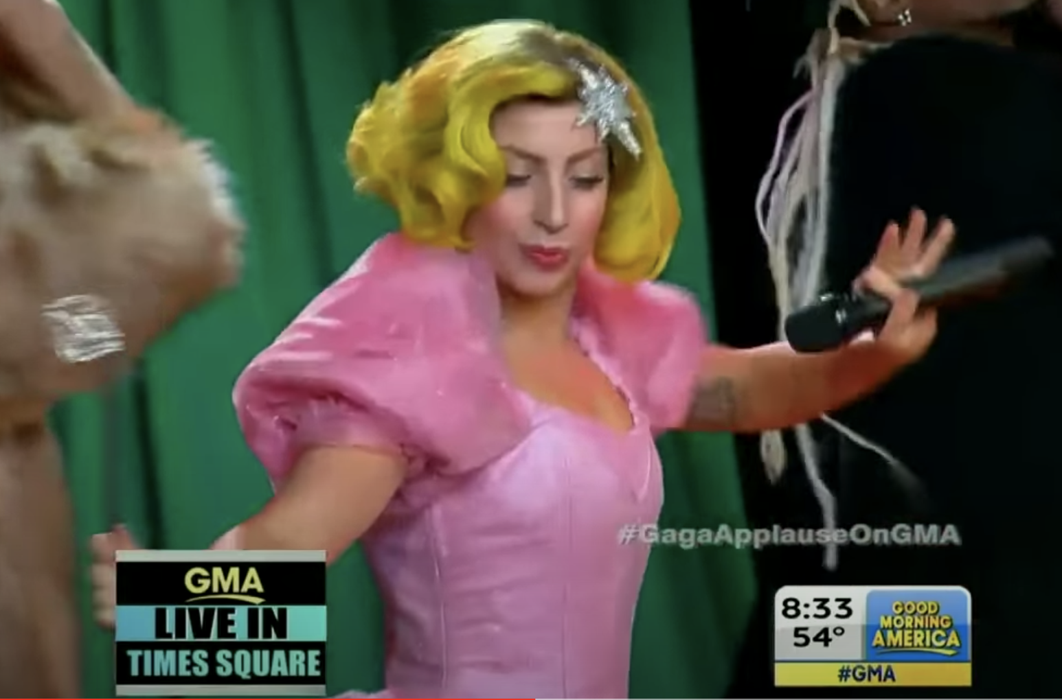 Gaga in a short green wig and a pink dress, along with a magic wand