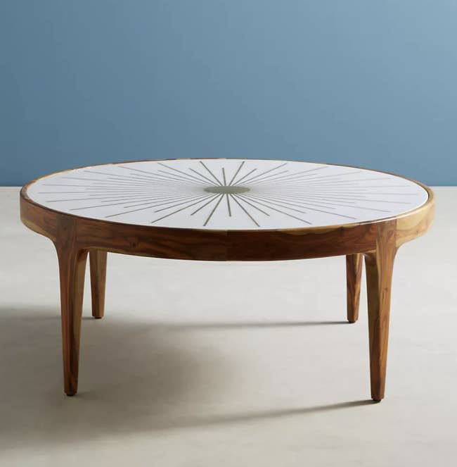 a brown rounded coffee table with a white table top and a gold starburst in the middle
