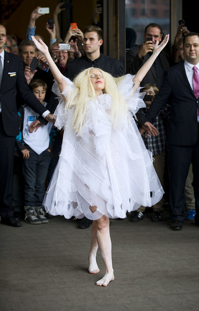 Gaga wearing a knee-length lace dress while doing a V with her arms