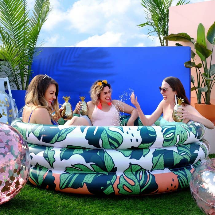 Three models sitting in inflatable sunning pool that&#x27;s bigger than a kiddie pool, but not too much larger than that