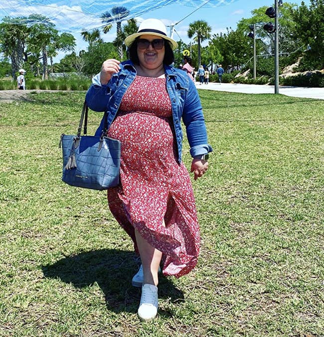 reviewer wearing dress in a red floral pattern with a denim jacket, a hat, and a purse
