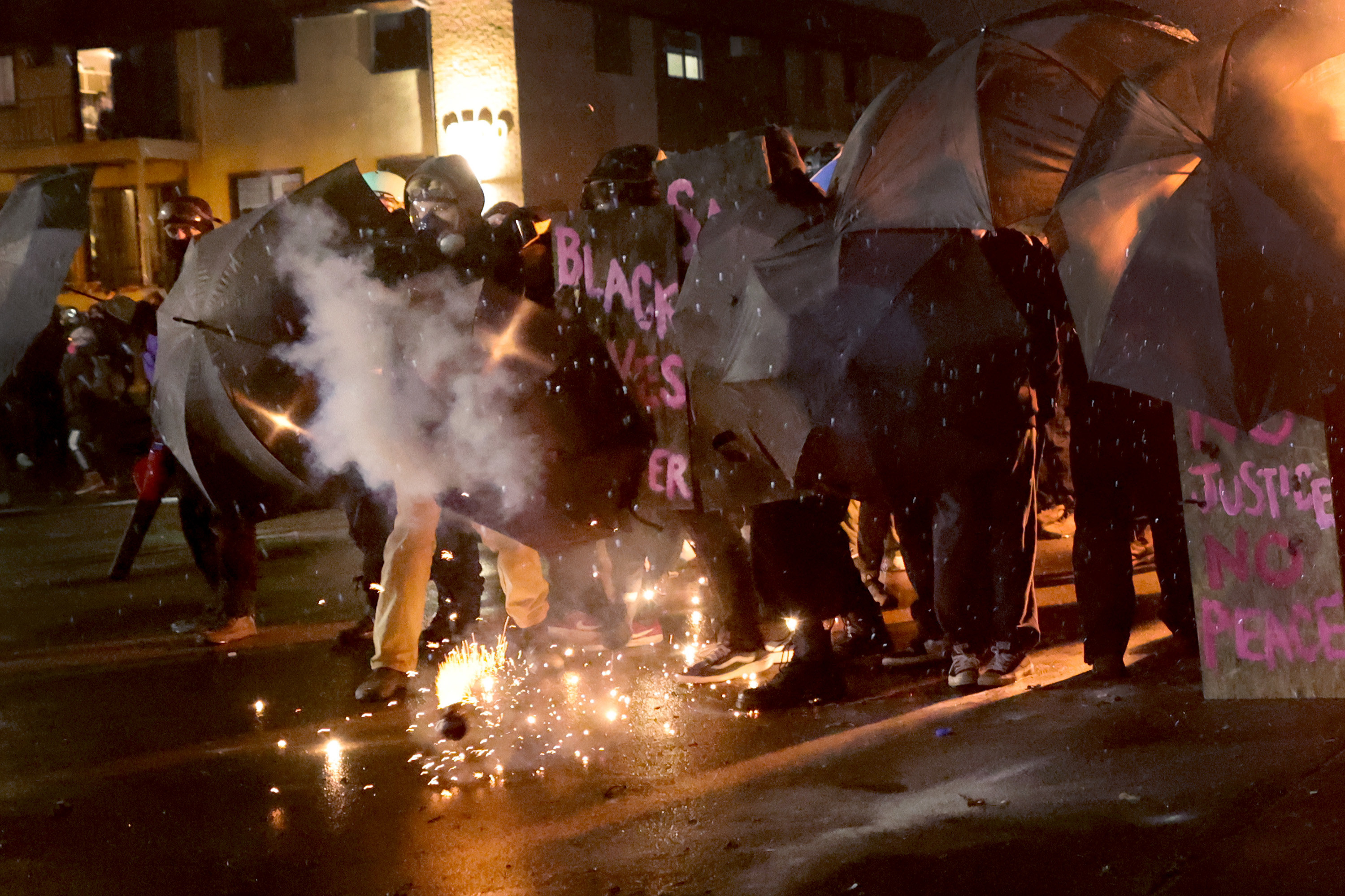 Protesters shield themselves with umbrellas as flash-bang grenades go off on the street at their feet