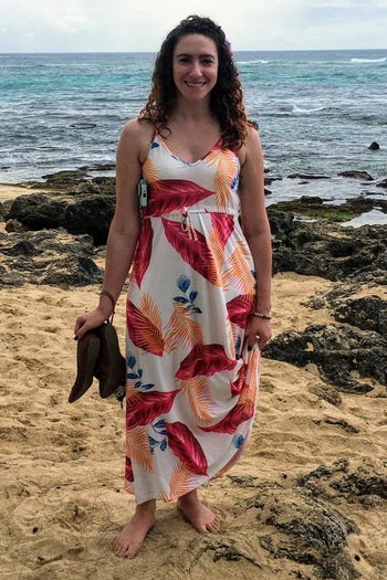 a reviewer wearing the dress in white with a pink and orange print on a beach
